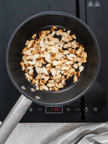 Almond slices being toasted to golden perfection in a small skillet, to add a nutty crunch to the salad.