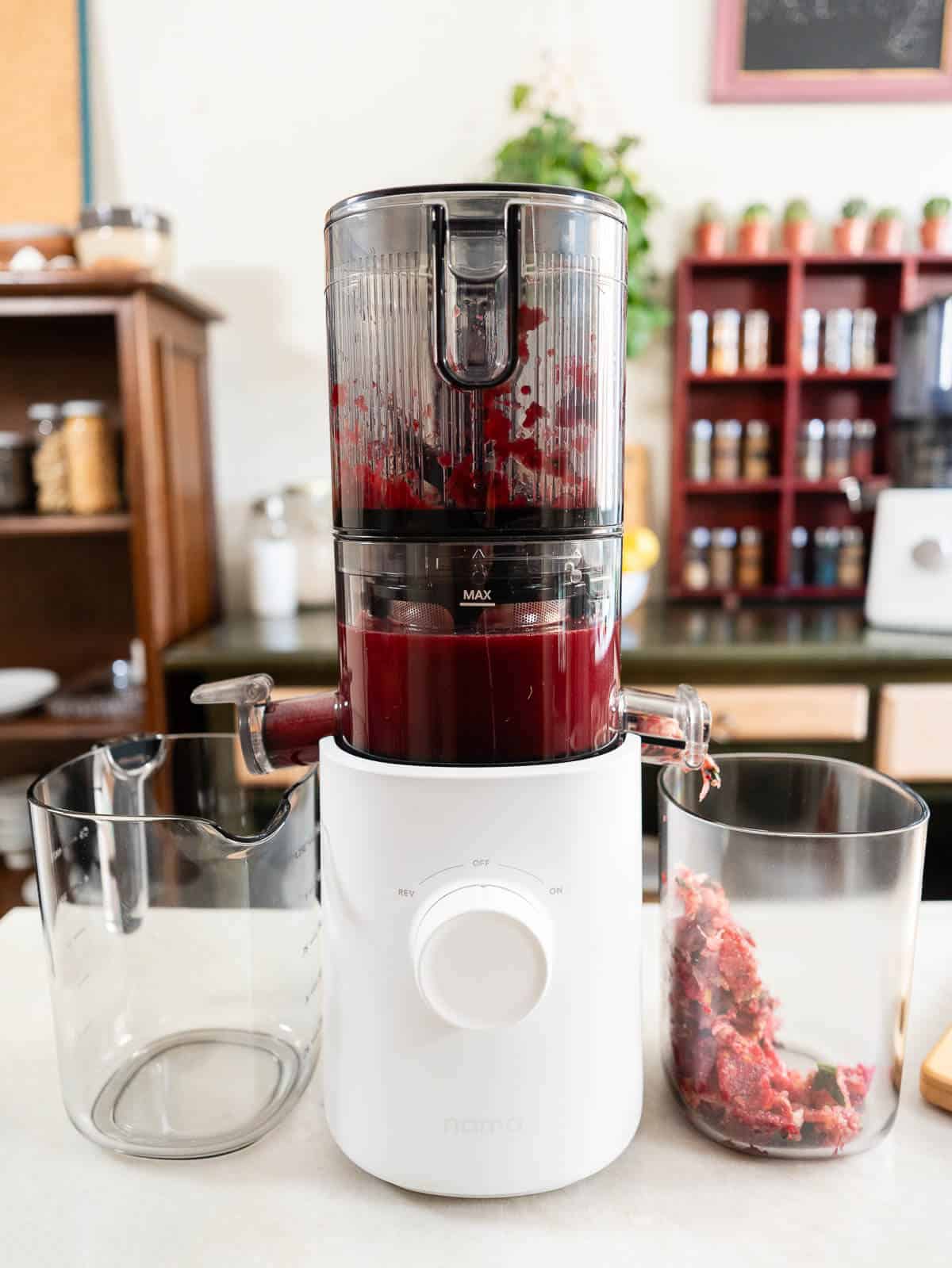 cold press juicer with juice in the chamber and pulp falling into the pulp container.