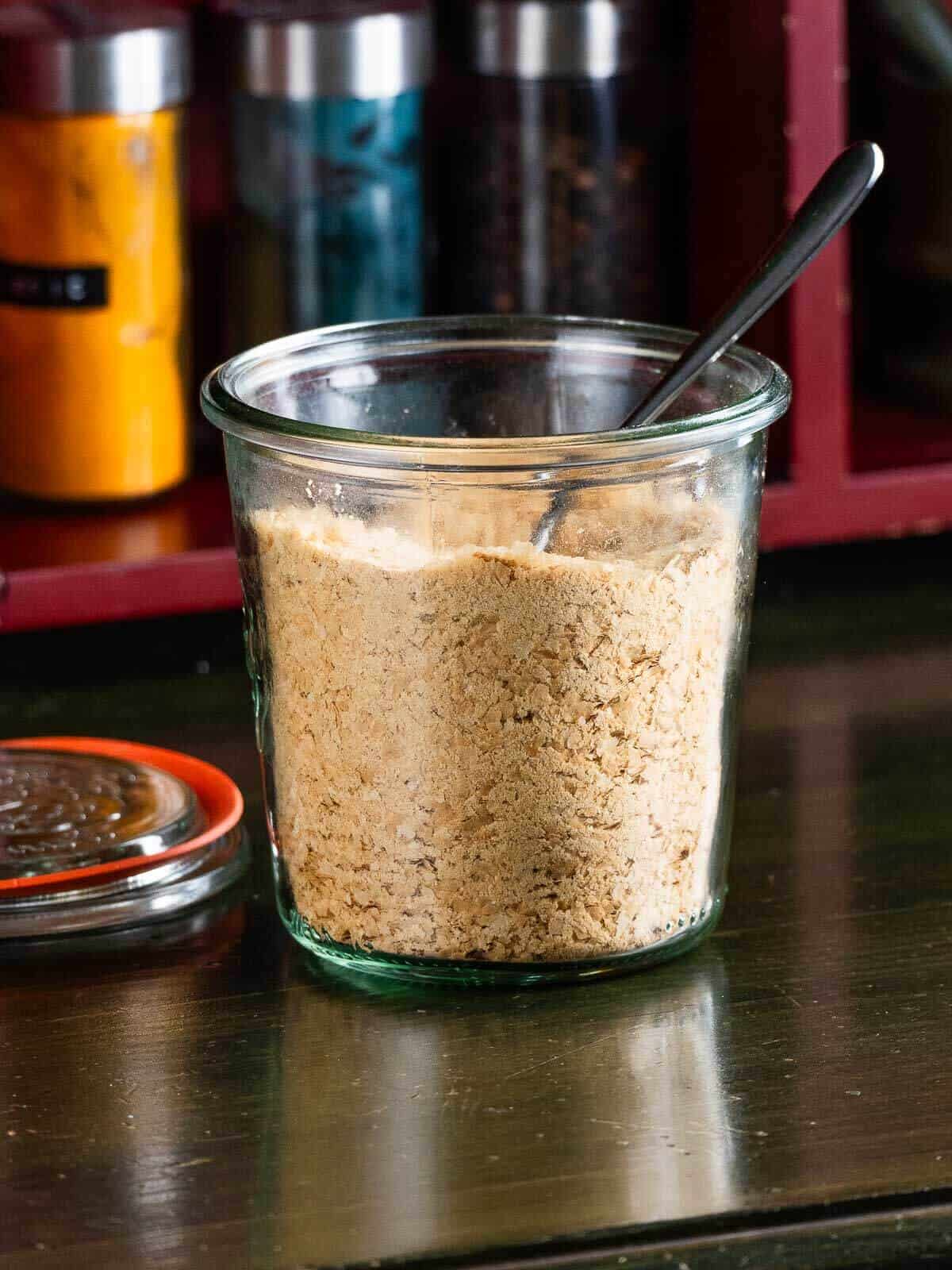 A close-up of a jar filled to the brim with nutritional yeast flakes, providing a detailed view of the texture and natural color of the flakes.