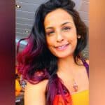 Natasha Gomez Akel headshot or selfie, smiling face head tilted. purple streaks in hair