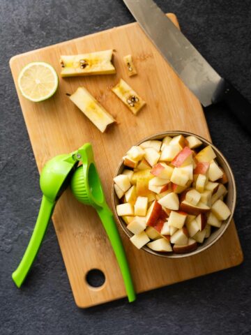 cored and cubed apples on a chopping board next to pressed lime.