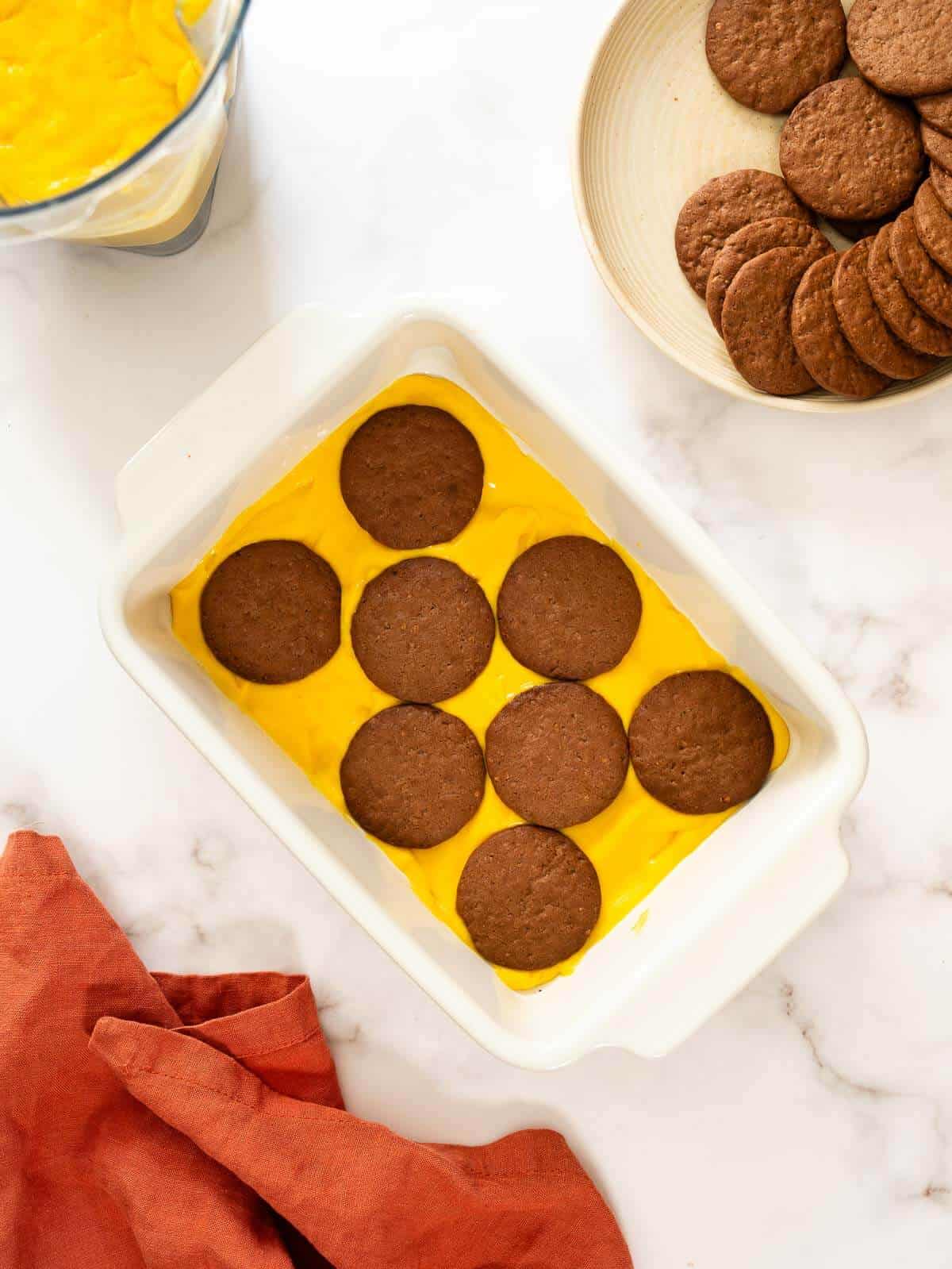 chocolate cookies on top of a pumpkin mixture layered on a baking dish.