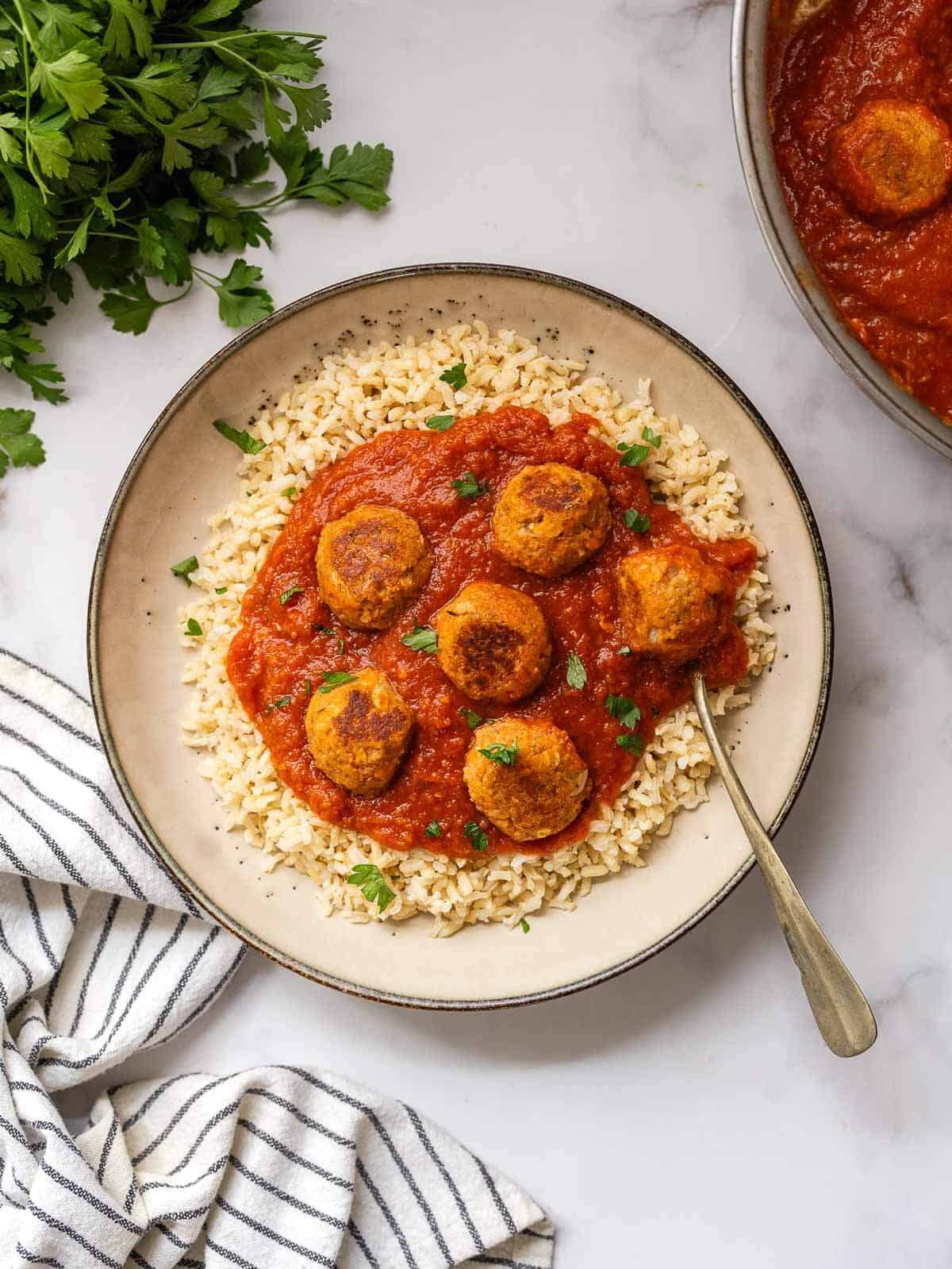 vegan meatballs with tomato sauce served over bran rice topped with chopped parsley.