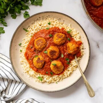 Top view of a bowl of vegan meatballs in marinara sauce, garnished with parsley.
