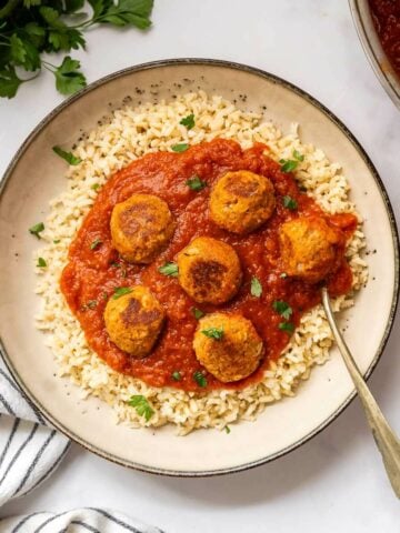Top view of a bowl of vegan meatballs in marinara sauce, garnished with parsley.