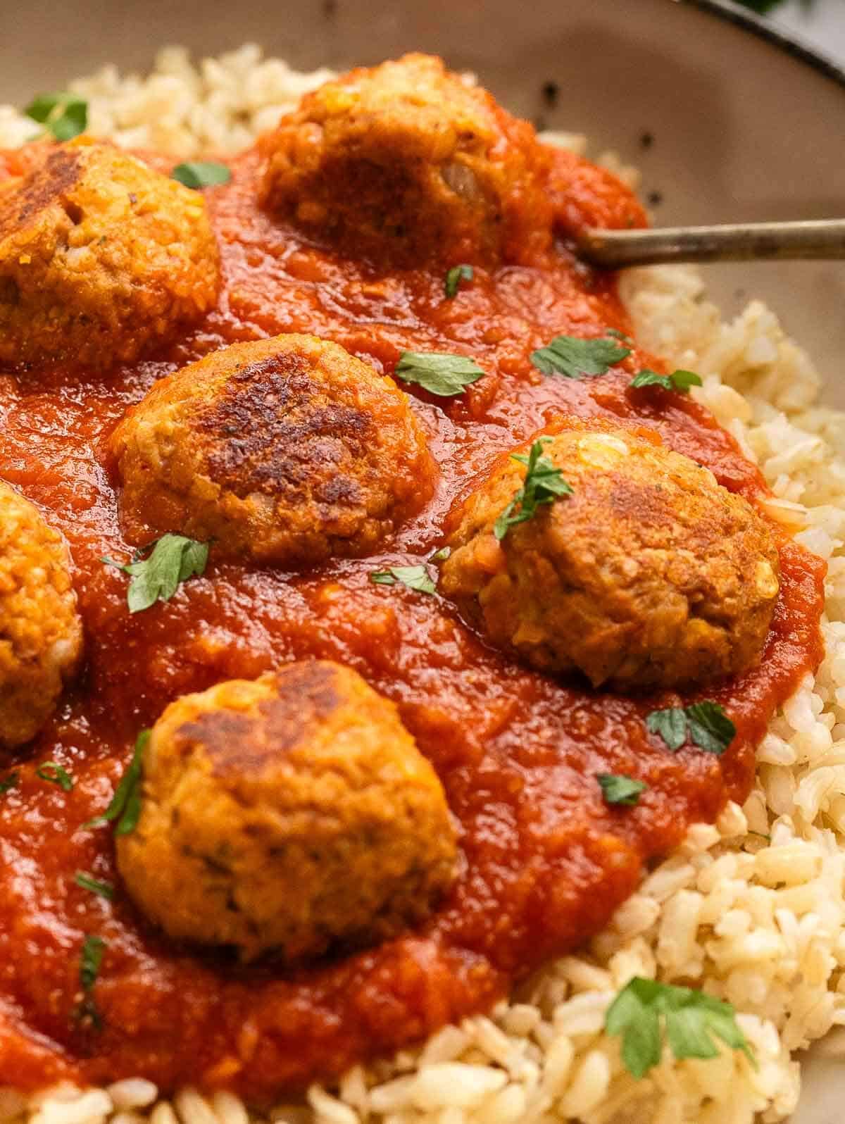 close up of vegan meatballs with tomato sauce served over bran rice.