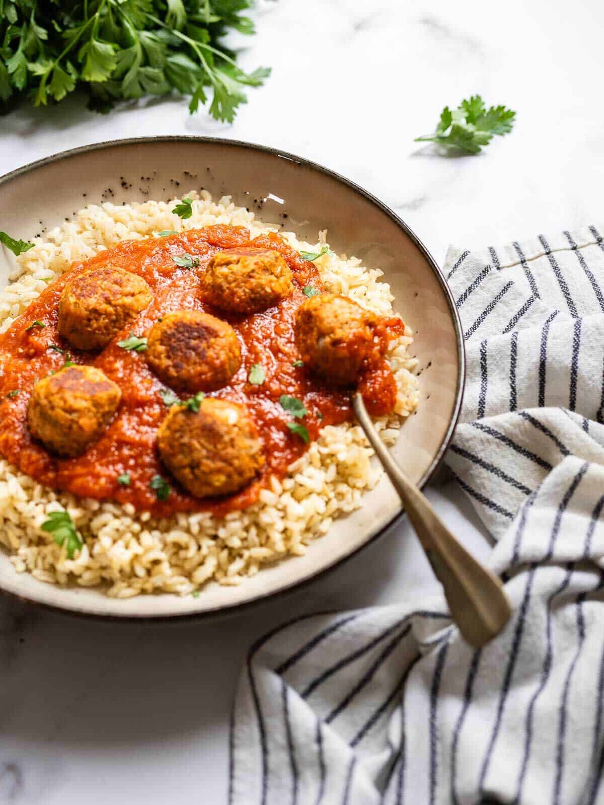 close up of vegan meatballs with tomato sauce served over bran rice.