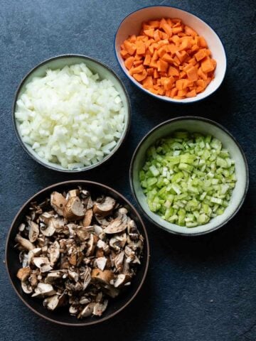 Chopped ingredients for the filling, including onions, carrots, celery, and mushrooms in separate bowls.