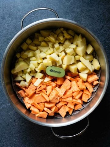 Chopped sweet potatoes and regular potatoes in a pot, ready for steaming.