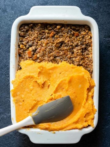 Spreading mashed sweet potatoes over the lentil filling in the baking dish.