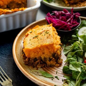 Another angle of the vegan shepherd's pie slice on a plate with salad and pickled red cabbage.