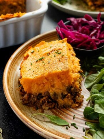 Another angle of the vegan shepherd's pie slice on a plate with salad and pickled red cabbage.