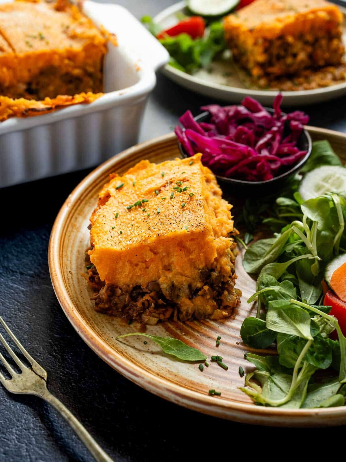 A serving of vegan shepherd's pie on a plate, accompanied by a fresh salad with cherry tomatoes and mixed greens.