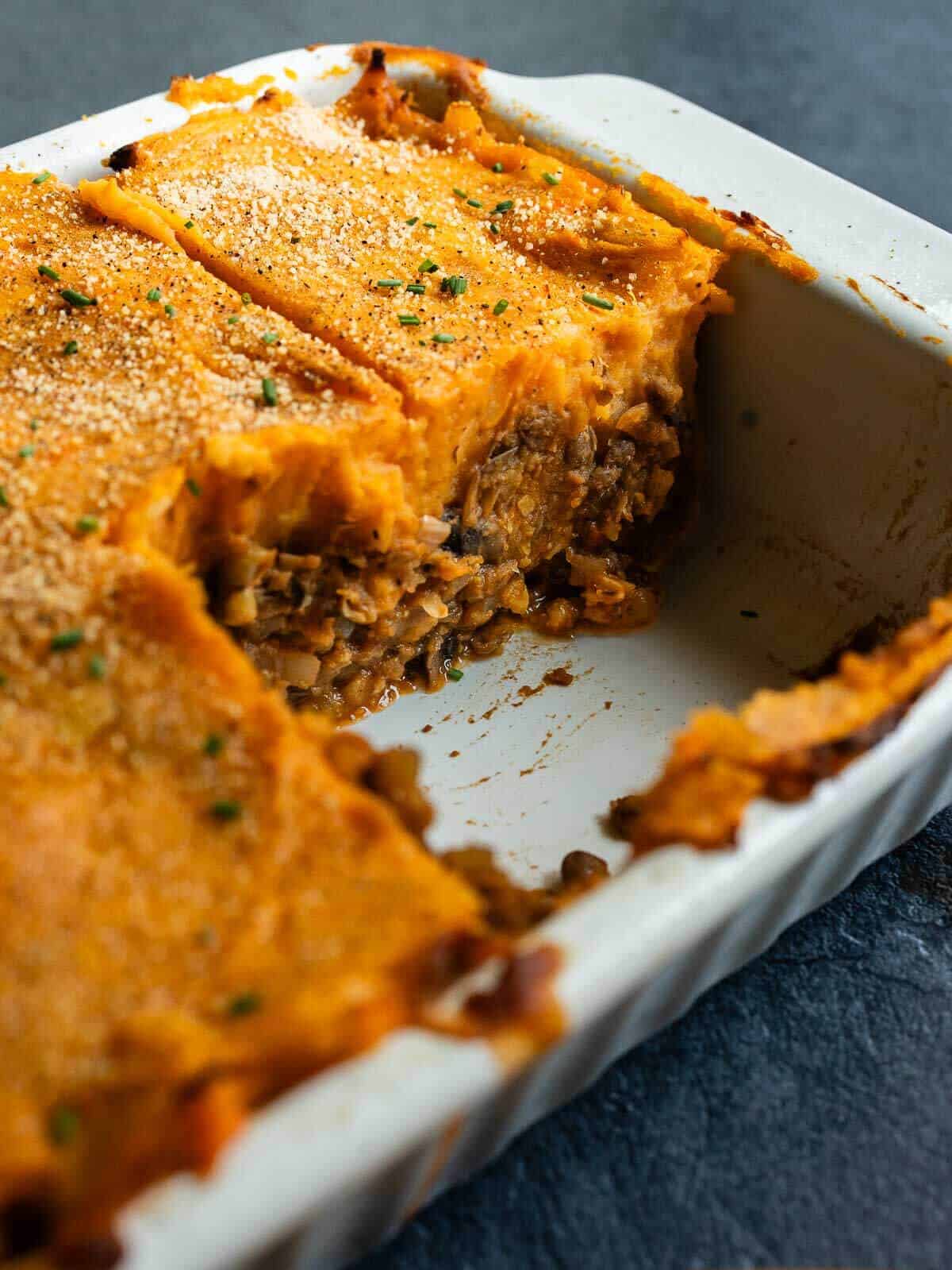 Sliced vegan shepherd's pie in a white baking dish, showing the layers of mashed sweet potatoes and lentil filling.